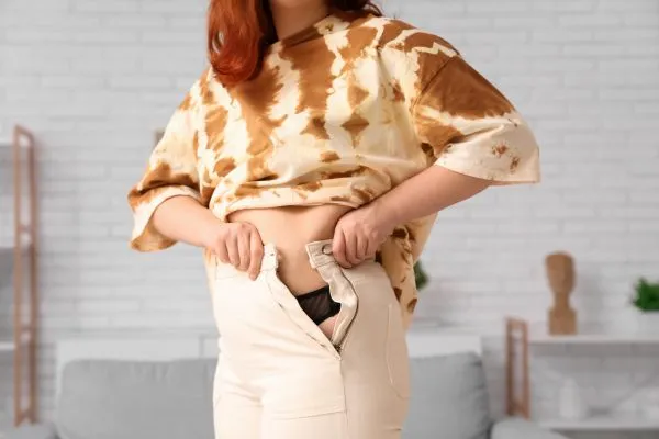 Image of woman trying to do her trousers up after pregnancy weight gain Sussex