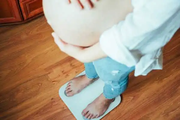 Image of woman weighing herself and experiencing weight gain through pregnancy Sussex
